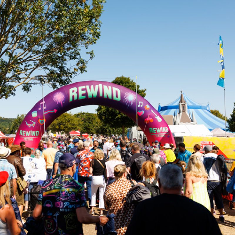 a banner saying Rewind over a crowd of people under a blue sky