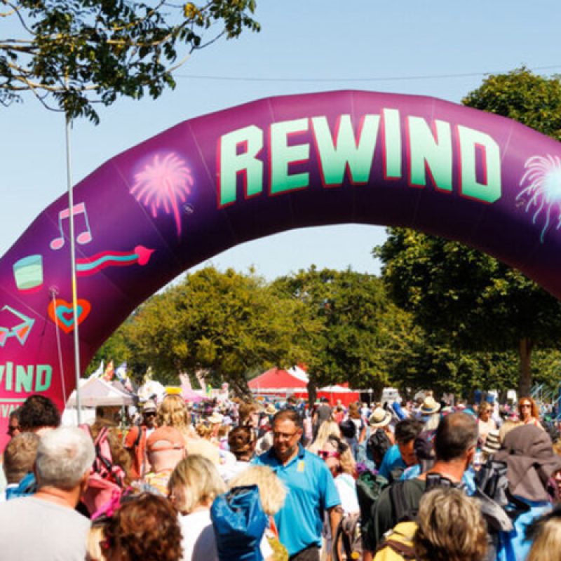 a banner saying Rewind over a crowd of people under a blue sky